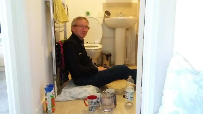 A man sitting on a bathroom floor, trying to appear composed during a pause between bouts of vomiting.