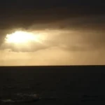 Sunset over the sea with sunbeams breaking through dark storm clouds.