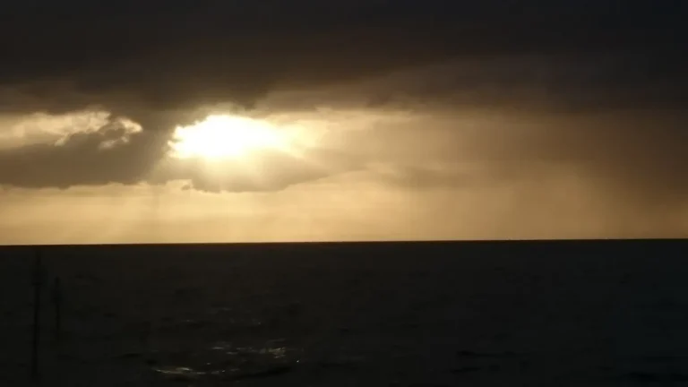 Sunset over the sea with sunbeams breaking through dark storm clouds.