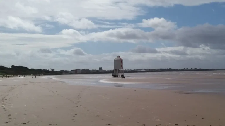 Low Lighthouse on the Beach in Burnham‑on‑Sea standing on wooden stilts at low tide, with wide wet sand and cloudy sky.