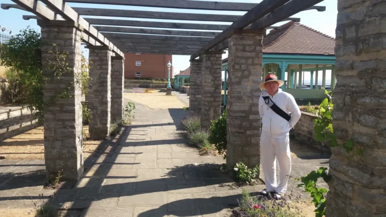 Person standing under a stone-and-wood pergola in a coastal garden area in Burnham‑on‑Sea.