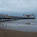 A cloudy seaside scene in Weston‑super‑Mare, with a lone swimmer in the water near the pier despite the rough sea.