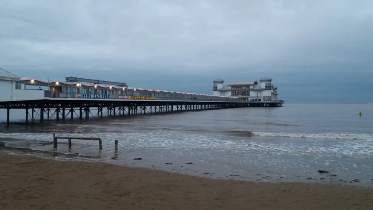 A cloudy seaside scene in Weston‑super‑Mare, with a lone swimmer in the water near the pier despite the rough sea.
