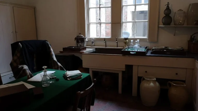A room in the former servants' quarters at Shugborough Estate with a sink, large vases, a table covered with green cloth, and two chairs.