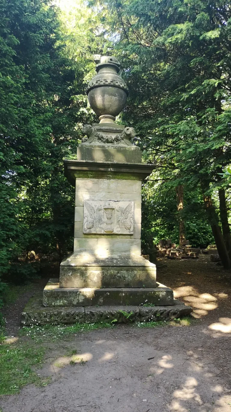 Cat’s Monument at Shugborough Estate, a stone pedestal with carved griffins and an urn in woodland.