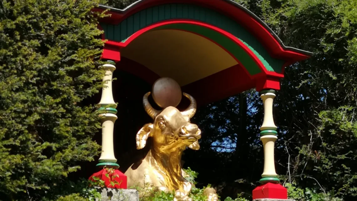 A golden statue of a bull in the garden of Biddulph Grange, holding a ball between its horns, surrounded by plants in the Chinese section of the garden.