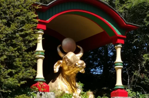 A golden statue of a bull in the garden of Biddulph Grange, holding a ball between its horns, surrounded by plants in the Chinese section of the garden.