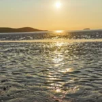 A golden sunset over the wet, rippled sands at Weston‑super‑Mare, with distant hills silhouetted on the horizon.