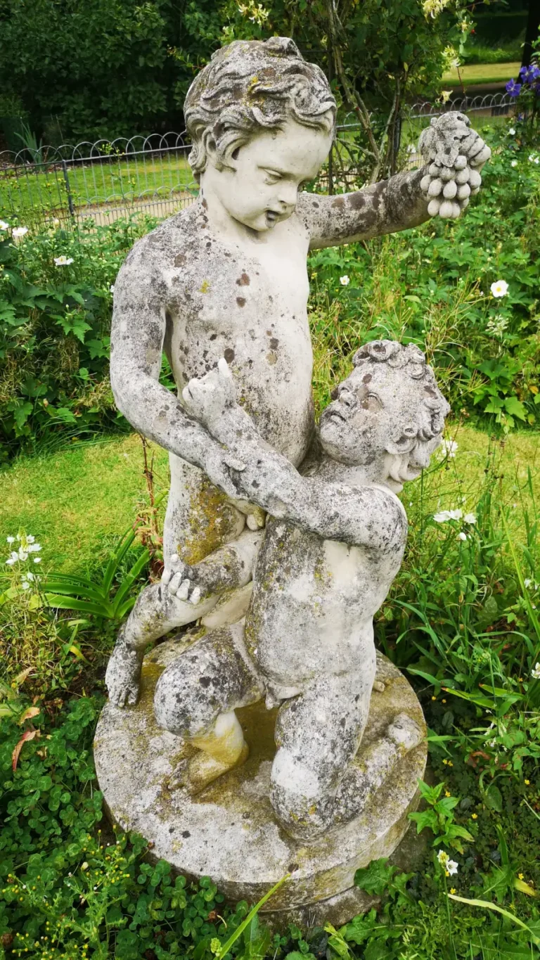 A weathered stone statue of two putti with grapes in the gardens of Shugborough Estate.
