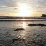 A romantic low‑angle sunset view taken just above the gentle waves in Weston‑super‑Mare, with Knightstone Island silhouetted on the right.