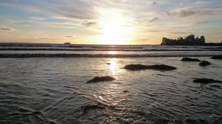 A romantic low‑angle sunset view taken just above the gentle waves in Weston‑super‑Mare, with Knightstone Island silhouetted on the right.