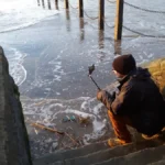 The blogger sits on the steps by the Marine Bay walkway in Weston‑super‑Mare, filming the sunset as waves rise against the stone.