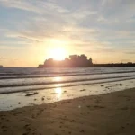 A romantic sunset over the beach in Weston‑super‑Mare, with gentle waves and Knightstone Island silhouetted on the horizon.