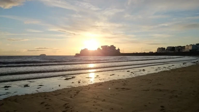 A romantic sunset over the beach in Weston‑super‑Mare, with gentle waves and Knightstone Island silhouetted on the horizon.