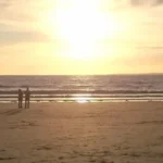 Two people stand on the beach in Weston‑super‑Mare at sunset, watching