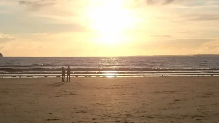 Two people stand on the beach in Weston‑super‑Mare at sunset, watching