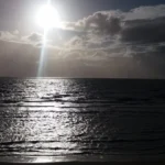 Sunlight breaking through clouds over the calm sea at Burnham‑on‑Sea, with gentle waves approaching the shore.