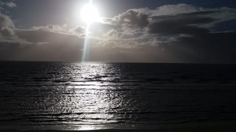 Sunlight breaking through clouds over the calm sea at Burnham‑on‑Sea, with gentle waves approaching the shore.