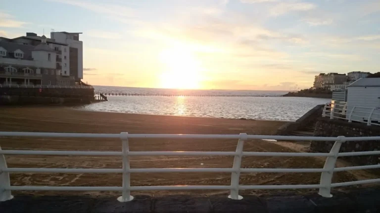 A sunset view from above Marine Lake Beach in Weston‑super‑Mare, with calm water, seaside buildings and a long breakwater on the horizon.