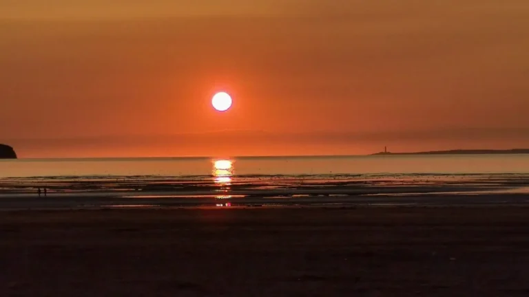 A warm sunset over the beach in Weston‑super‑Mare, with the lighthouse silhouetted against the glowing horizon.