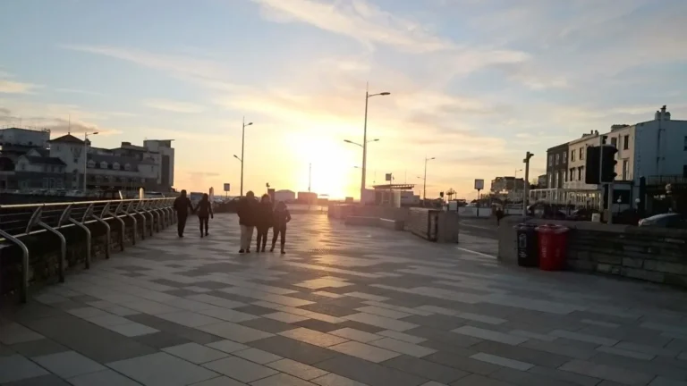 A sunset view from the promenade in Weston‑super‑Mare, looking toward Marine Bay with people walking along the waterfront.