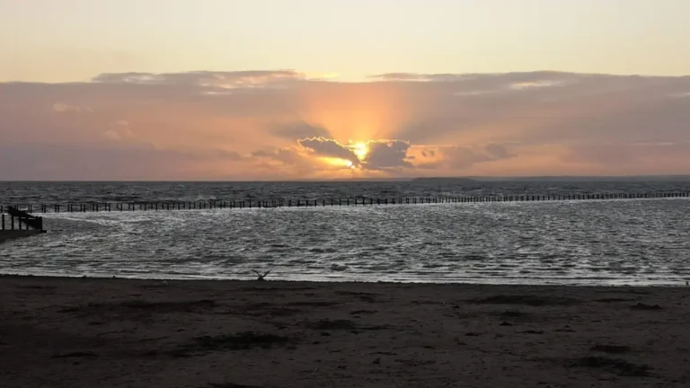 A warm sunset over the beach in Weston‑super‑Mare, with gentle waves and distant hills silhouetted on the horizon.