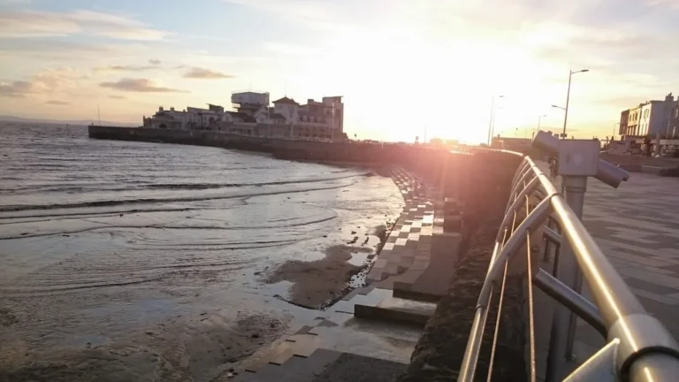 A sunset view from the promenade in Weston‑super‑Mare, looking toward Knightstone Island with a viewing telescope by the railings.