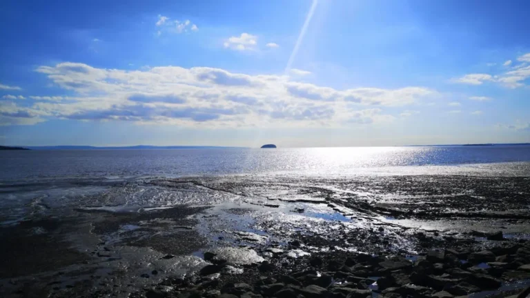 View from the road at Marine Lake towards the sea at low tide, with the water reflecting the sunlight in Weston-super-Mare.