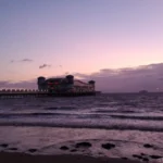 The Grand Pier in Weston‑super‑Mare illuminated at twilight, stretching over the calm sea beneath a purple‑pink sky.