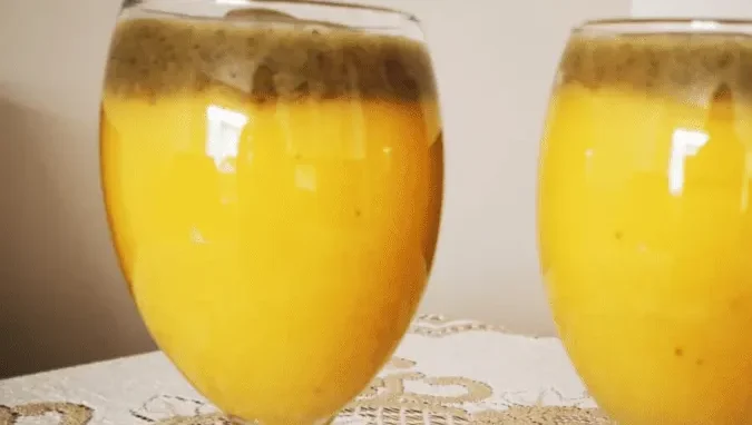 Two glasses of orange juice with a frothy layer of apple juice, standing on a table with a patterned tablecloth.