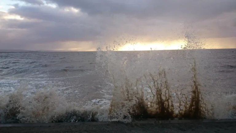 Waves crashing against the seawall in Burnham‑on‑Sea at sunset, with spray rising into the air.