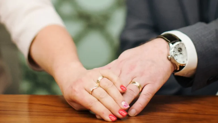 The hands of a newly married couple, with their wedding rings prominently displayed.