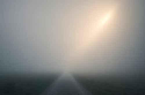A foggy path stretching into the distance, with a ray of light breaking through — a quiet image of uncertainty and hope.